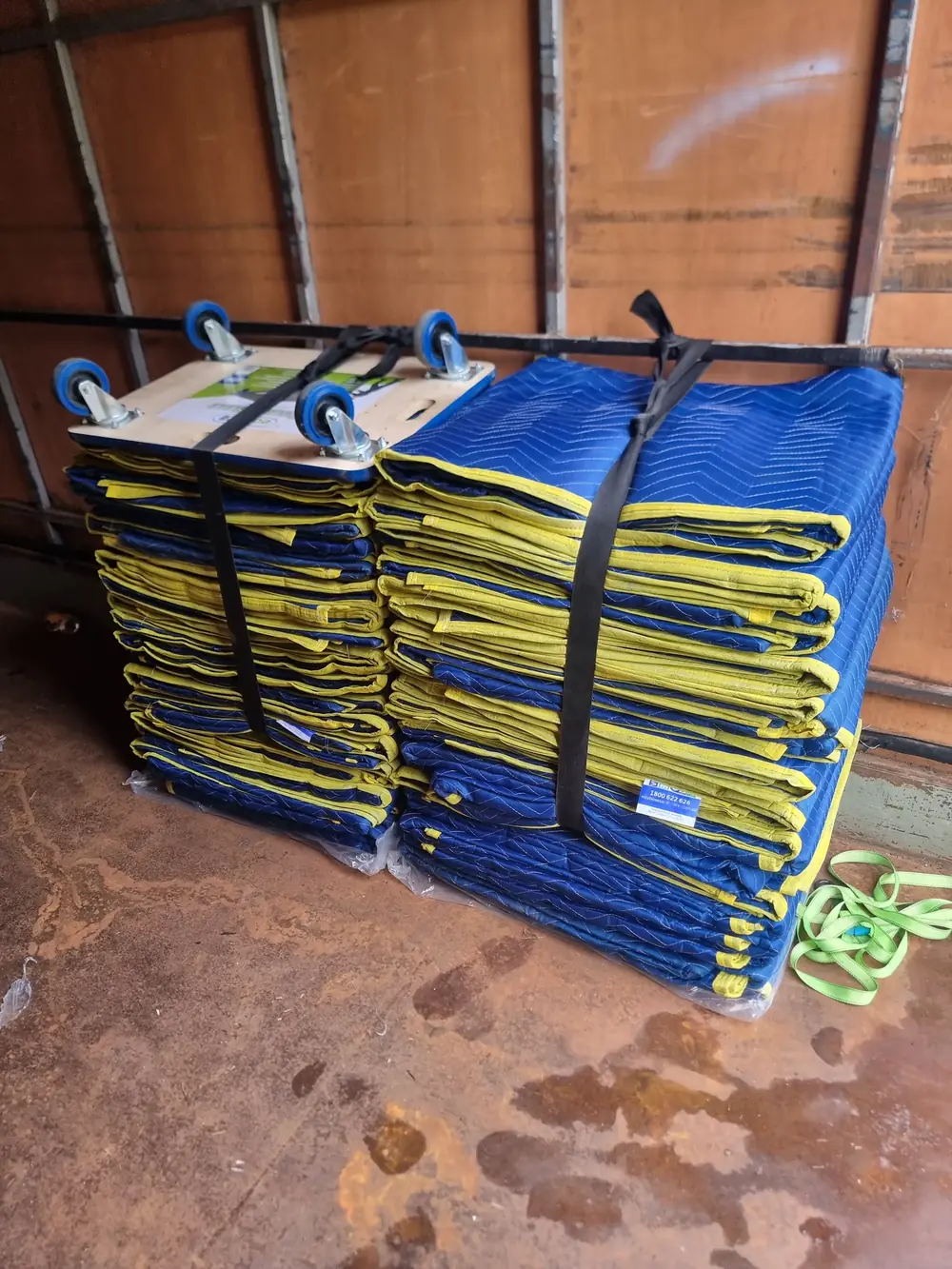 Stacks of blue and yellow moving blankets secured with tie-down straps
