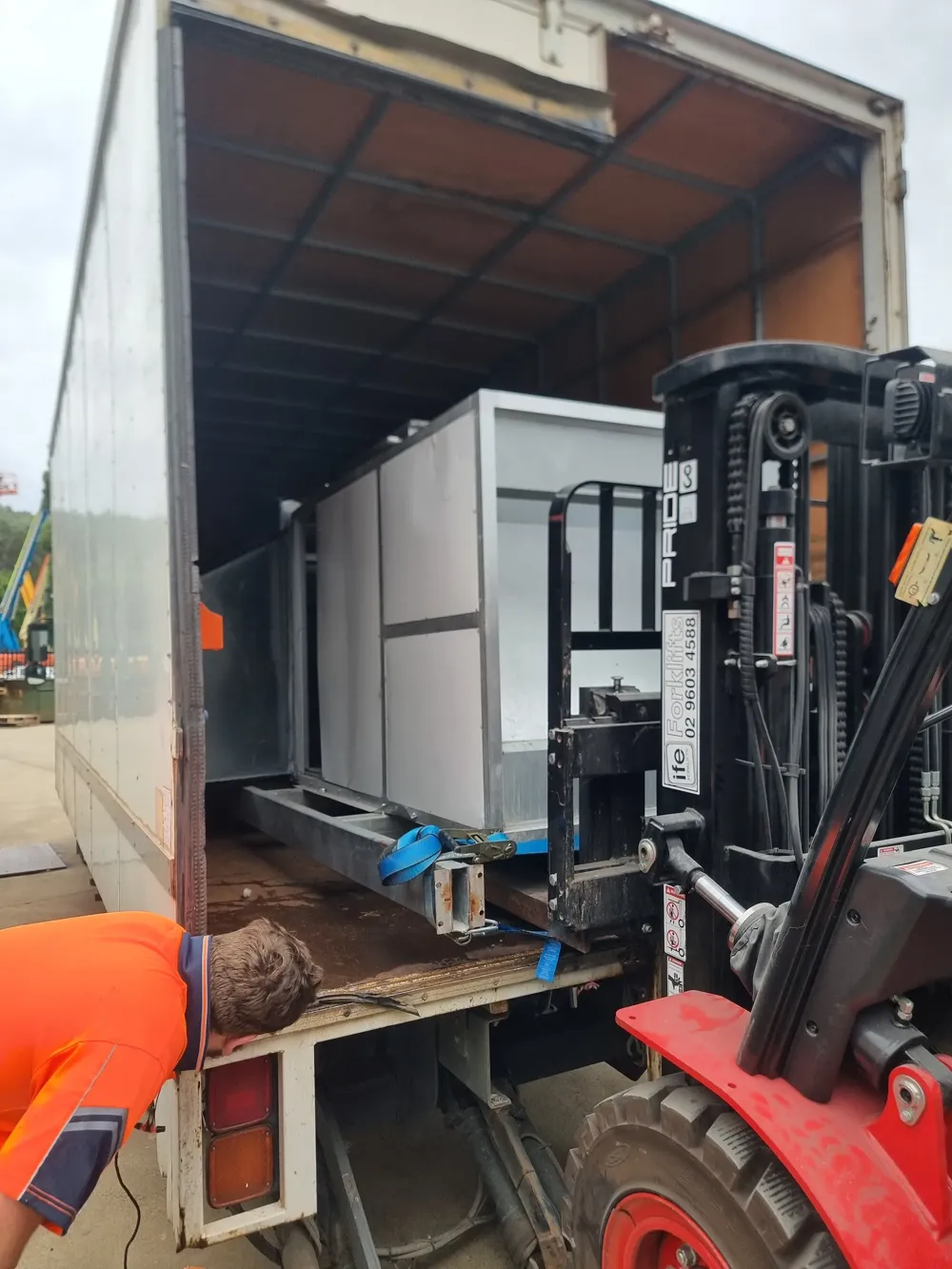 Forklift loading a white cabinet into a freight truck